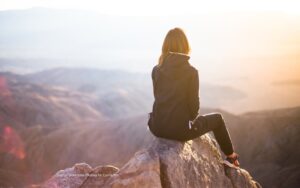 Woman sitting on a mountain top and considering the guiding question behind her desire to change her life.